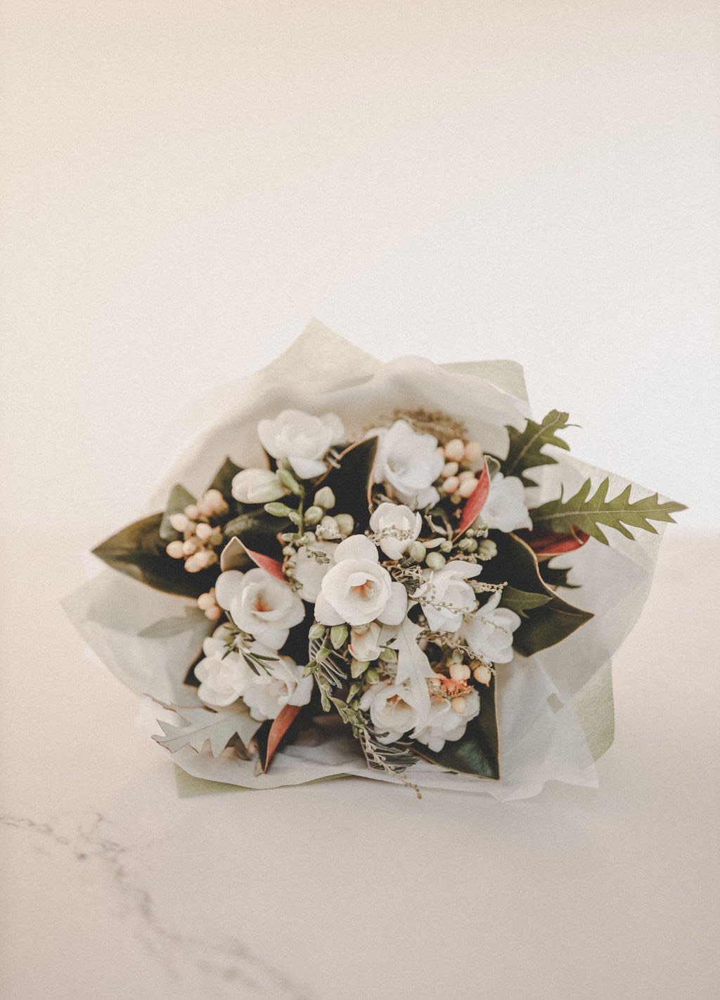 Elegant white floral bouquet with greenery and wrapped in white paper – perfect for weddings or special occasions