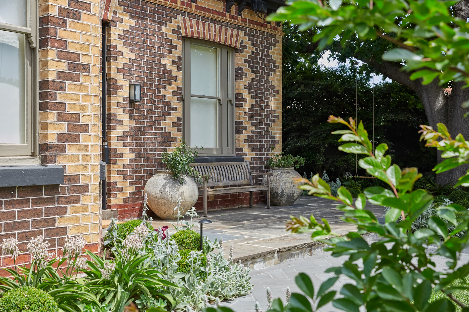 Brick façade with potted plants and a gravel path bordered by soft green planting