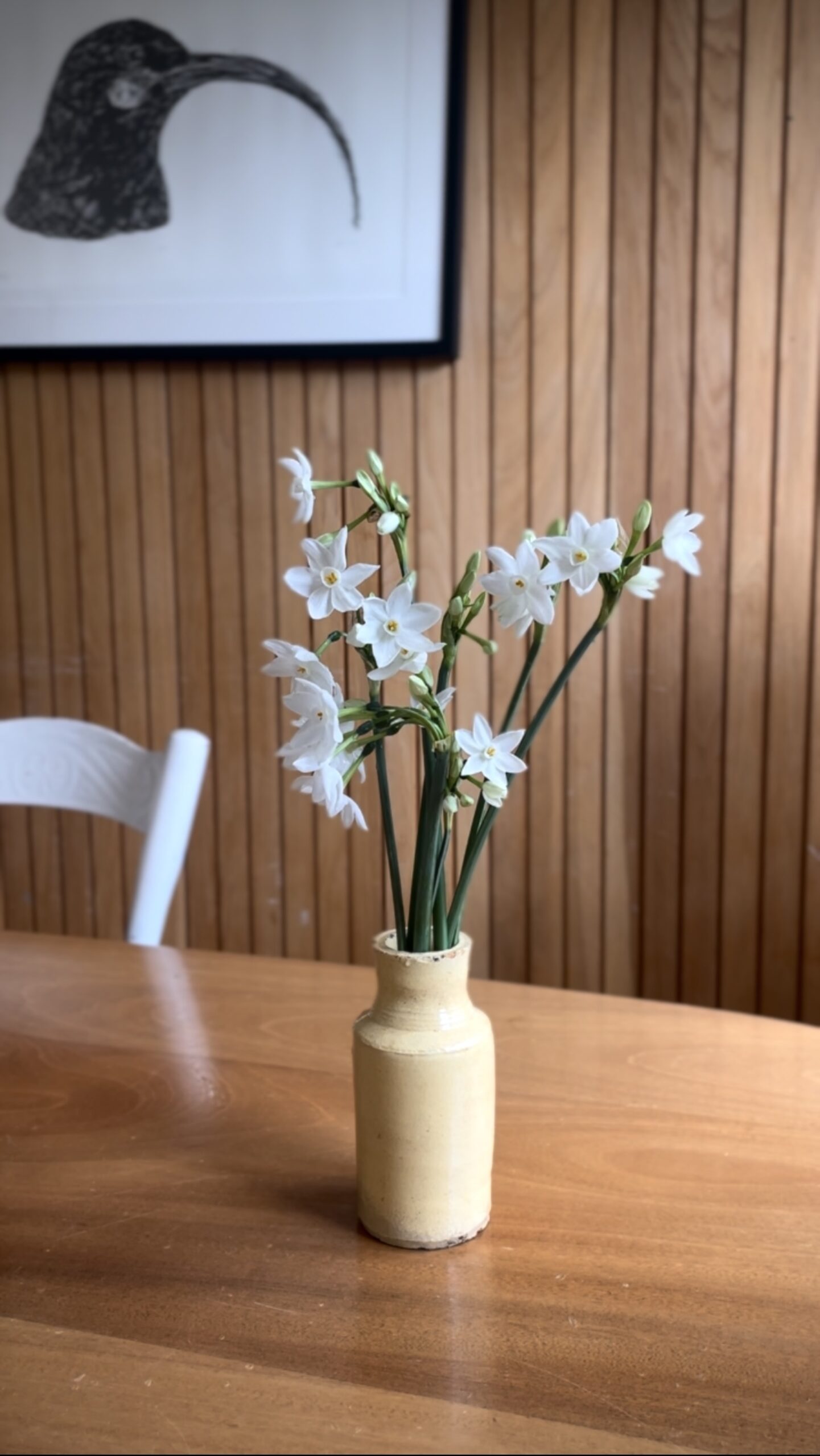 Indoor floral arrangement with daffodils Fresh daffodil arrangement in a tall vase on a wooden dining table with framed artwork.