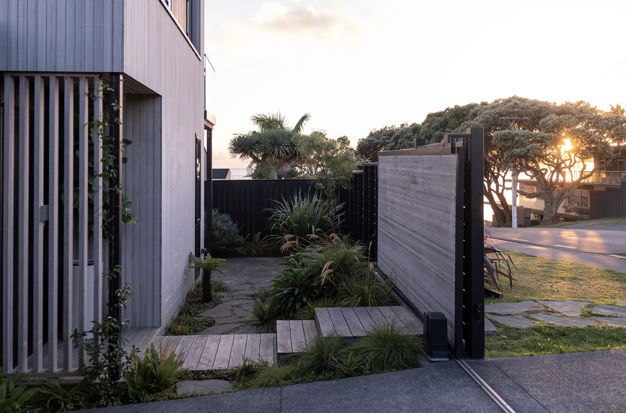 Modern garden entrance with concrete path and ornamental grasses at sunset