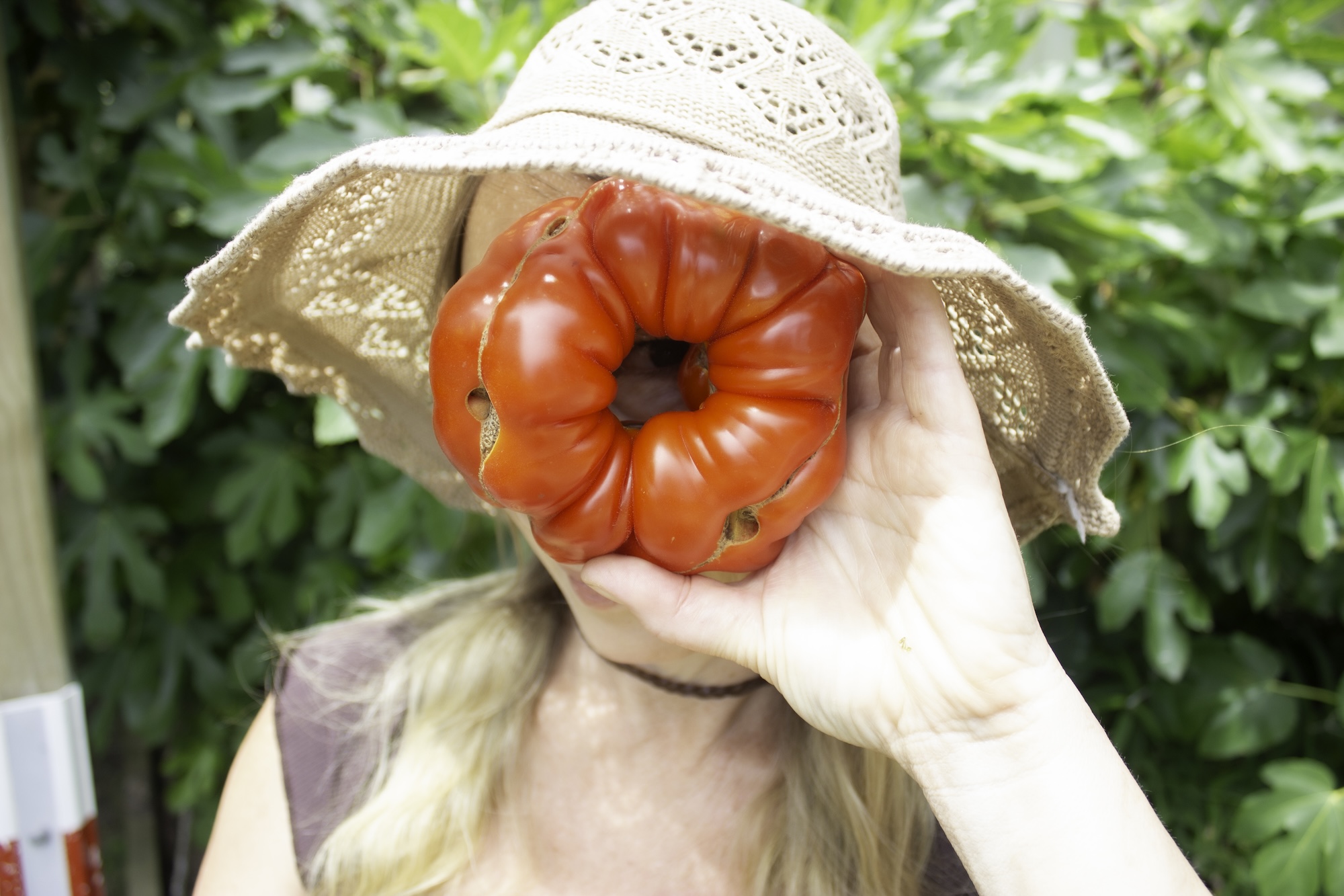 Abylene Chalmers playfully holding large red heirloom tomato in front of her face