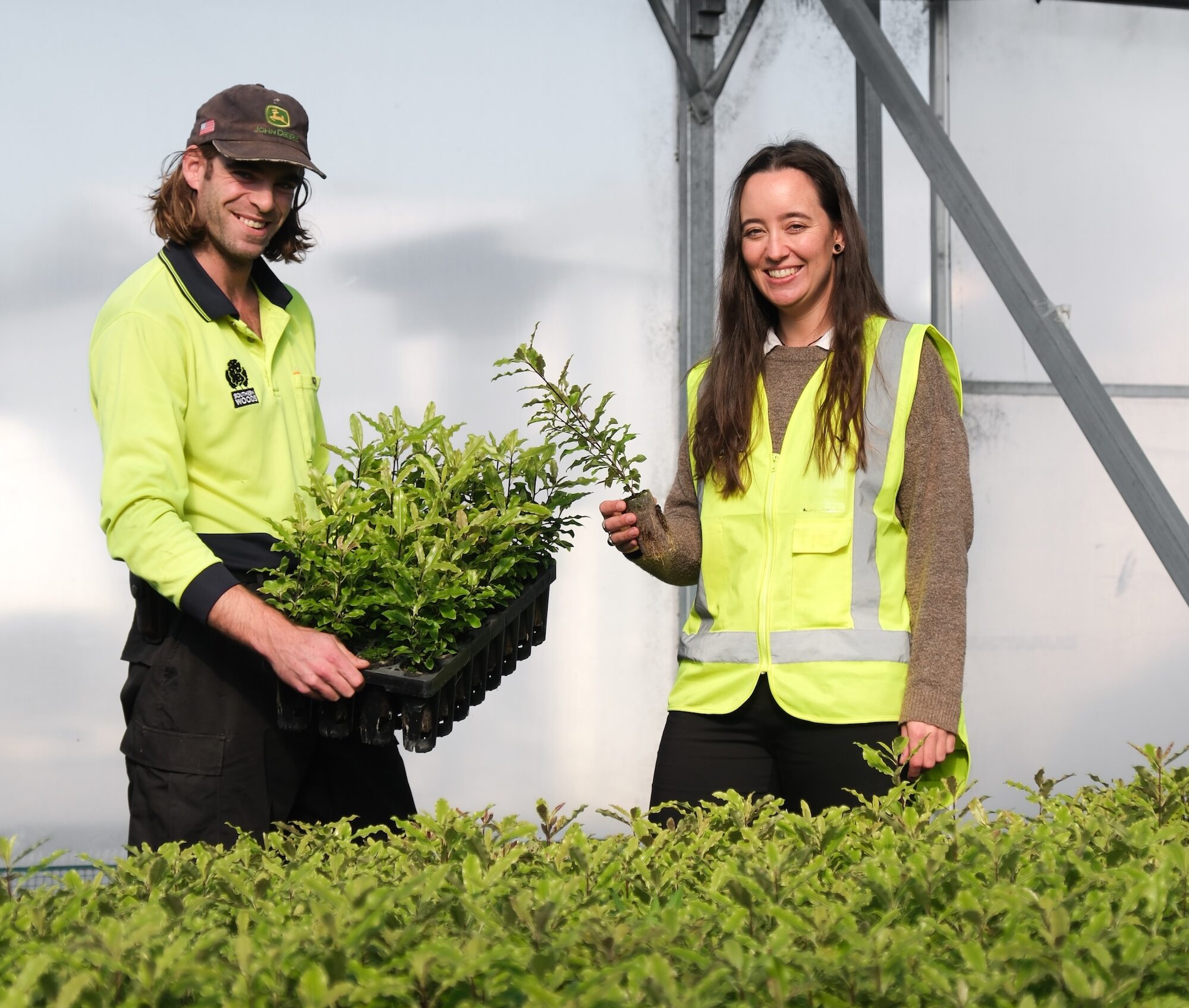 Nursery staff smiling with trays of young native plants in greenhouse