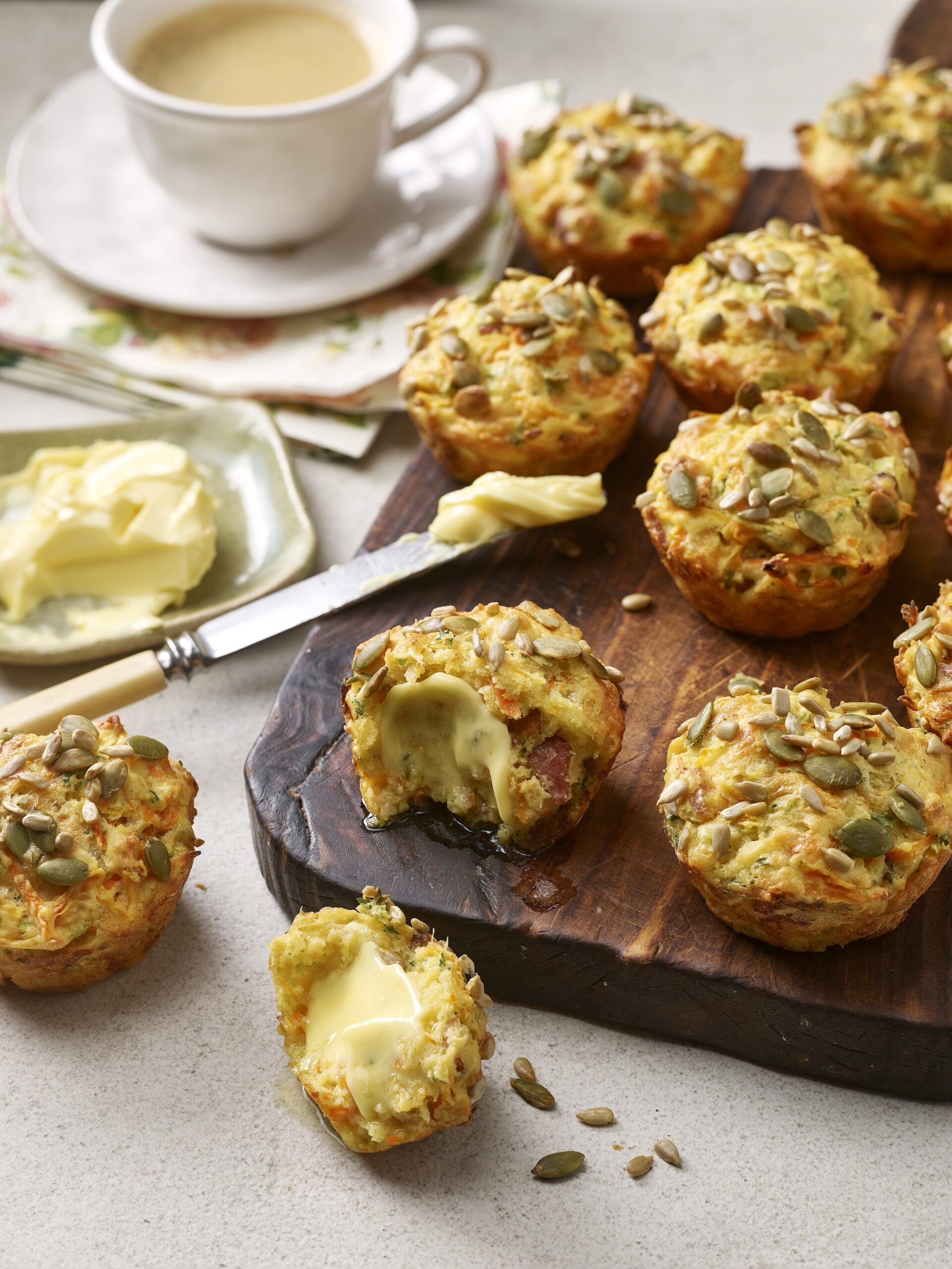 Freshly baked savoury bacon and vegetable muffins served with butter on a rustic wooden board – easy homemade snack recipe