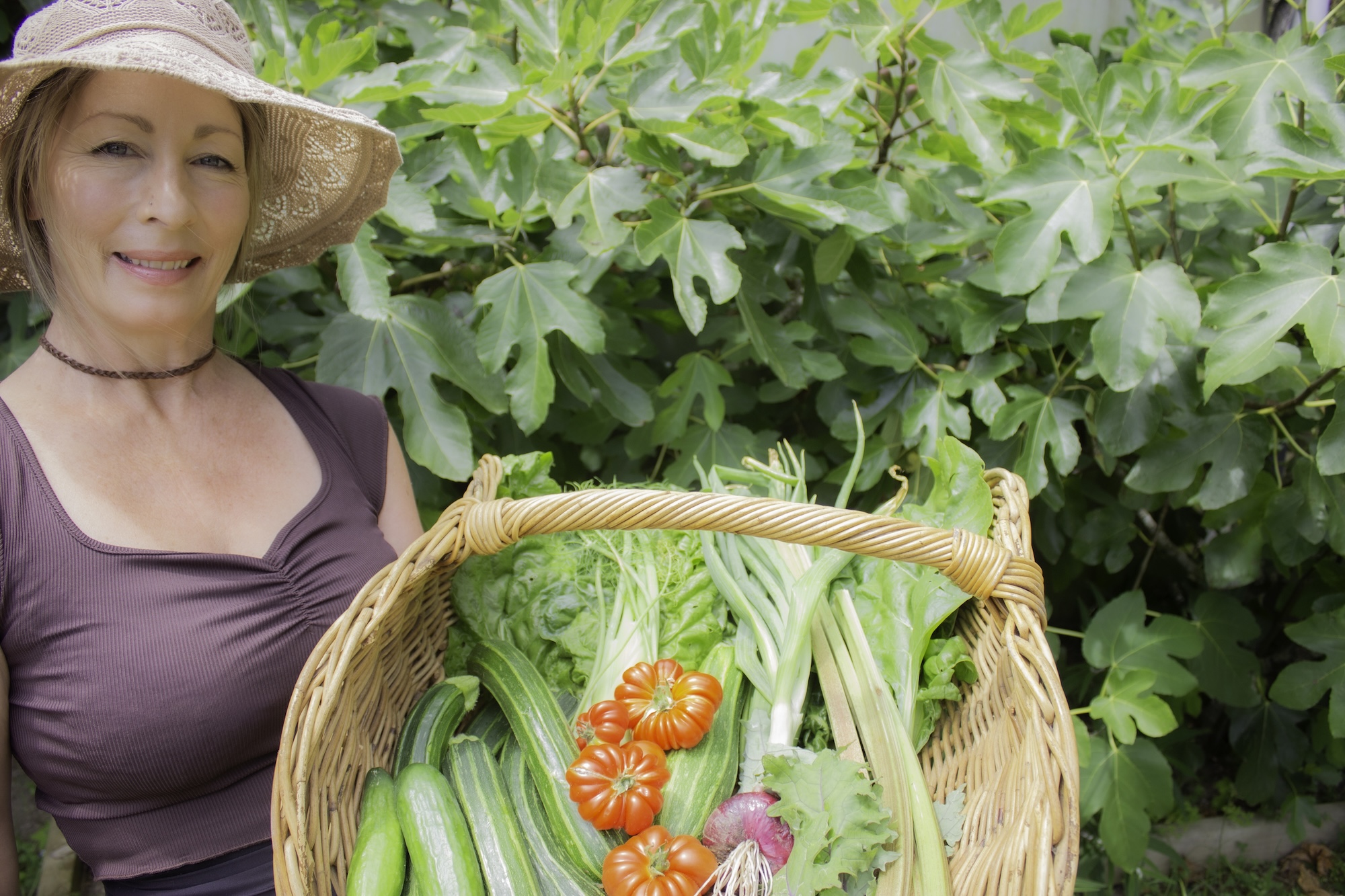 Abylene Chalmers holding a wicker basket filled with homegrown cucumbers, greens, and tomatoes