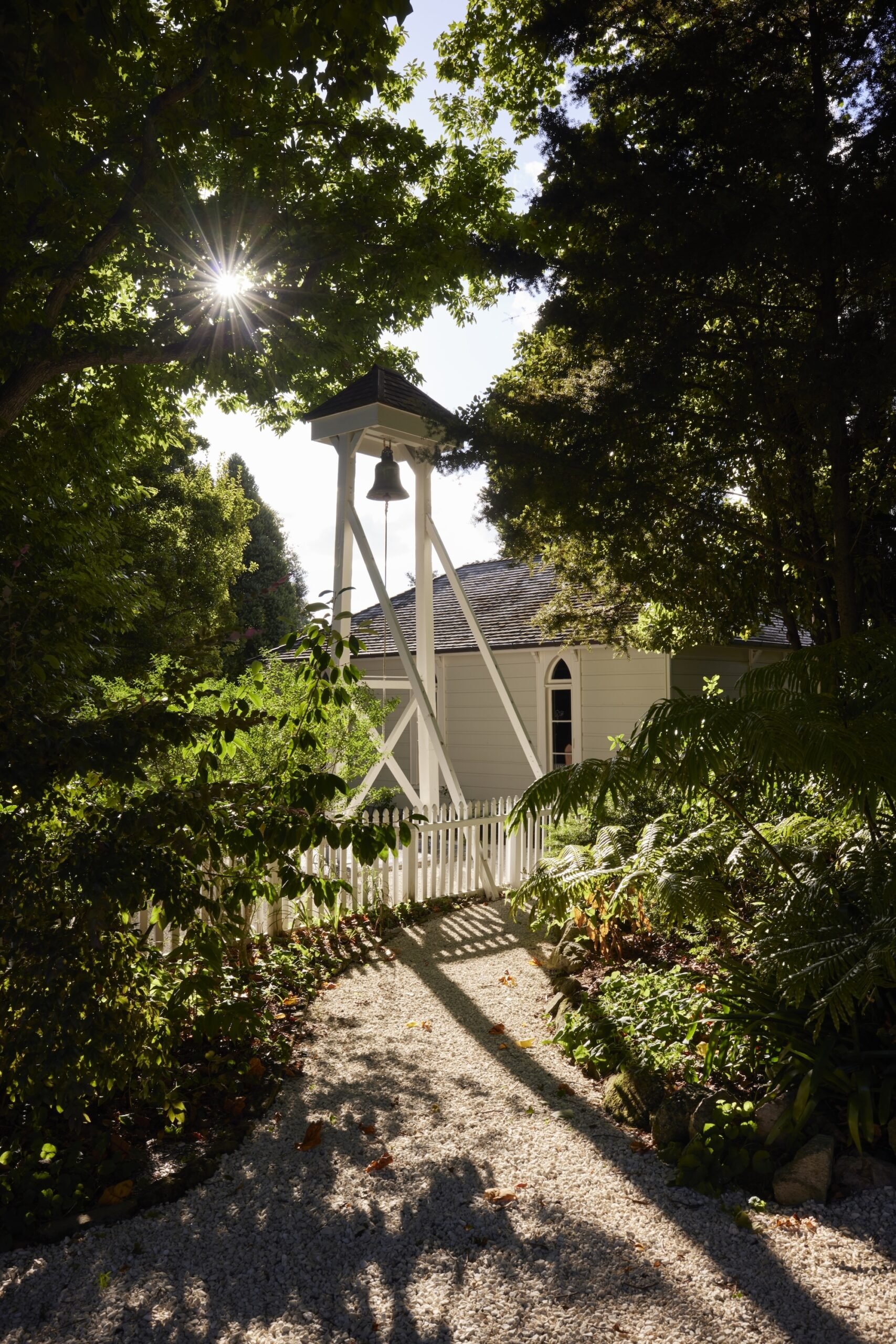 A gravel path leading toward a historic villa with sunlight filtering through the trees.