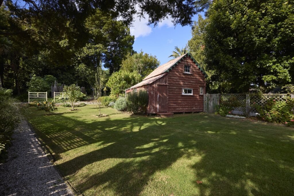 Charming red-brick cottage nestled in a heritage garden with surrounding trees.