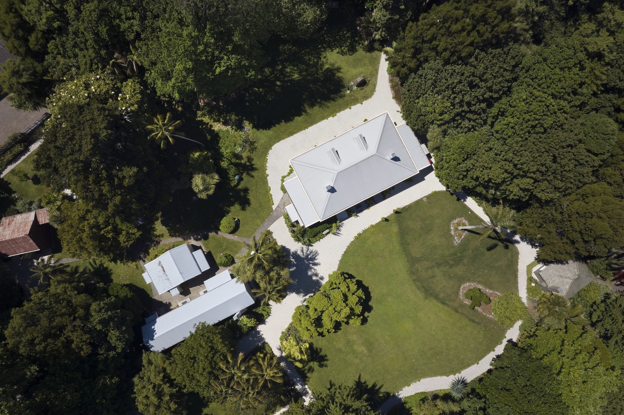 Drone view of a heritage estate with white gravel driveways, gardens, and surrounding trees.