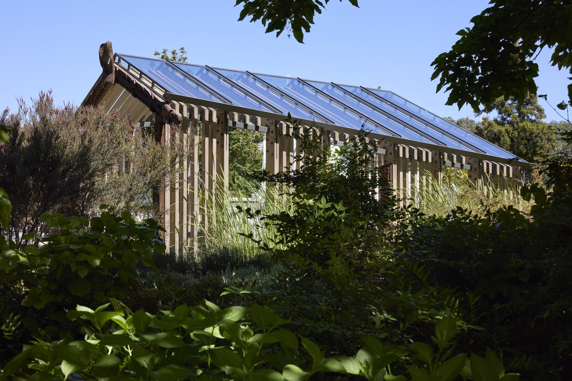 Quaint wooden garden cottage with pitched roof set among trees and stone landscaping.