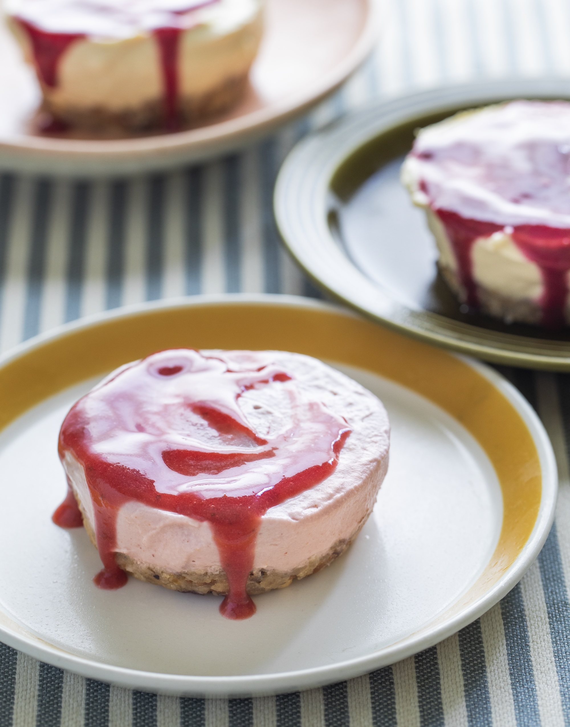 Cheesecake with red berry sauce drizzle sitting on yellow rimmed plate