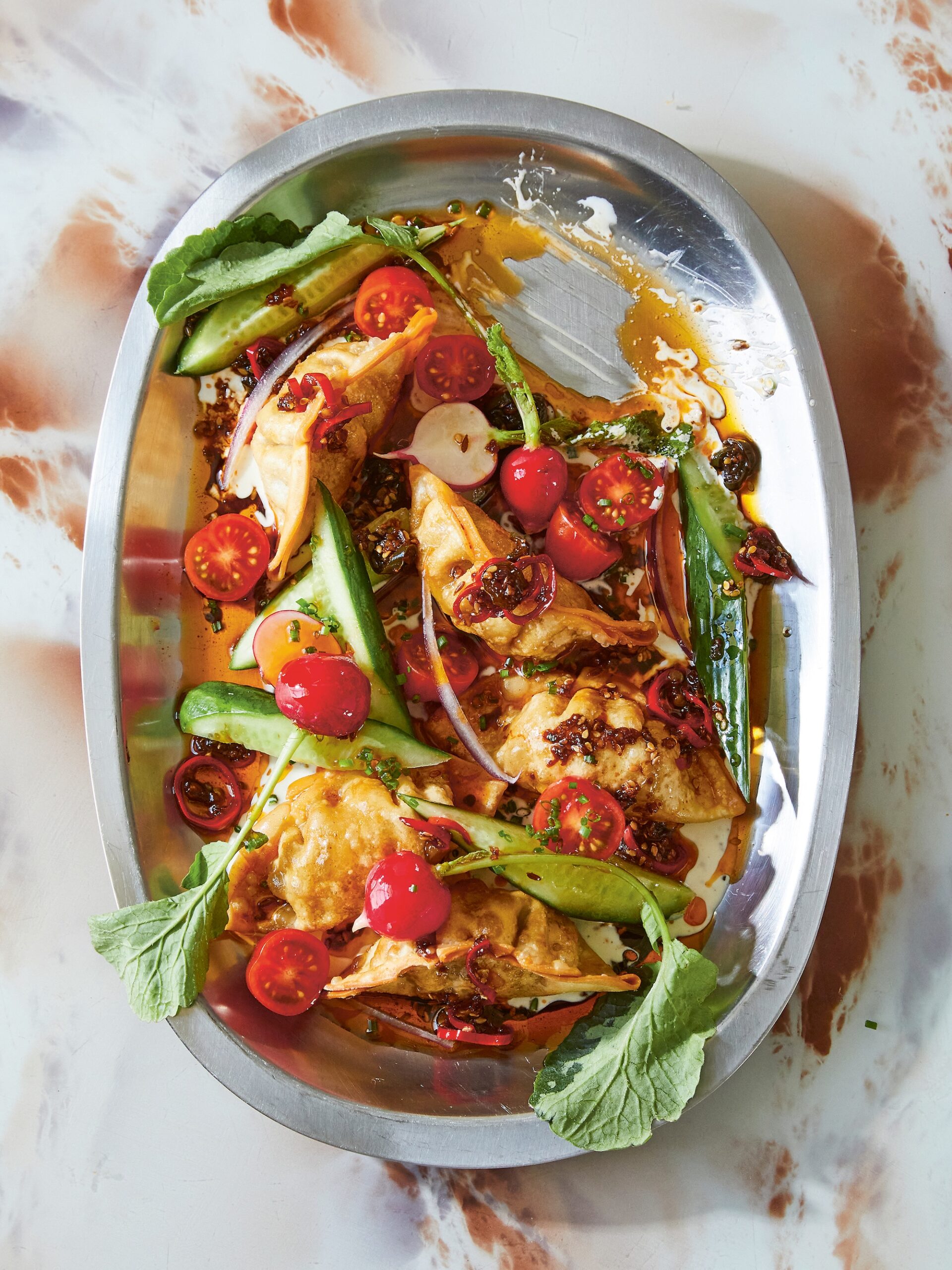 A colourful platter of dumplings and salad leaves topped with cherry tomatoes and sauce