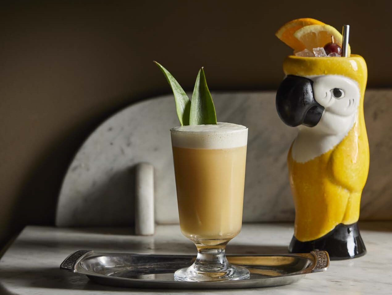 Pina colada cocktail served alongside tropical bird figurine cocktail glass
