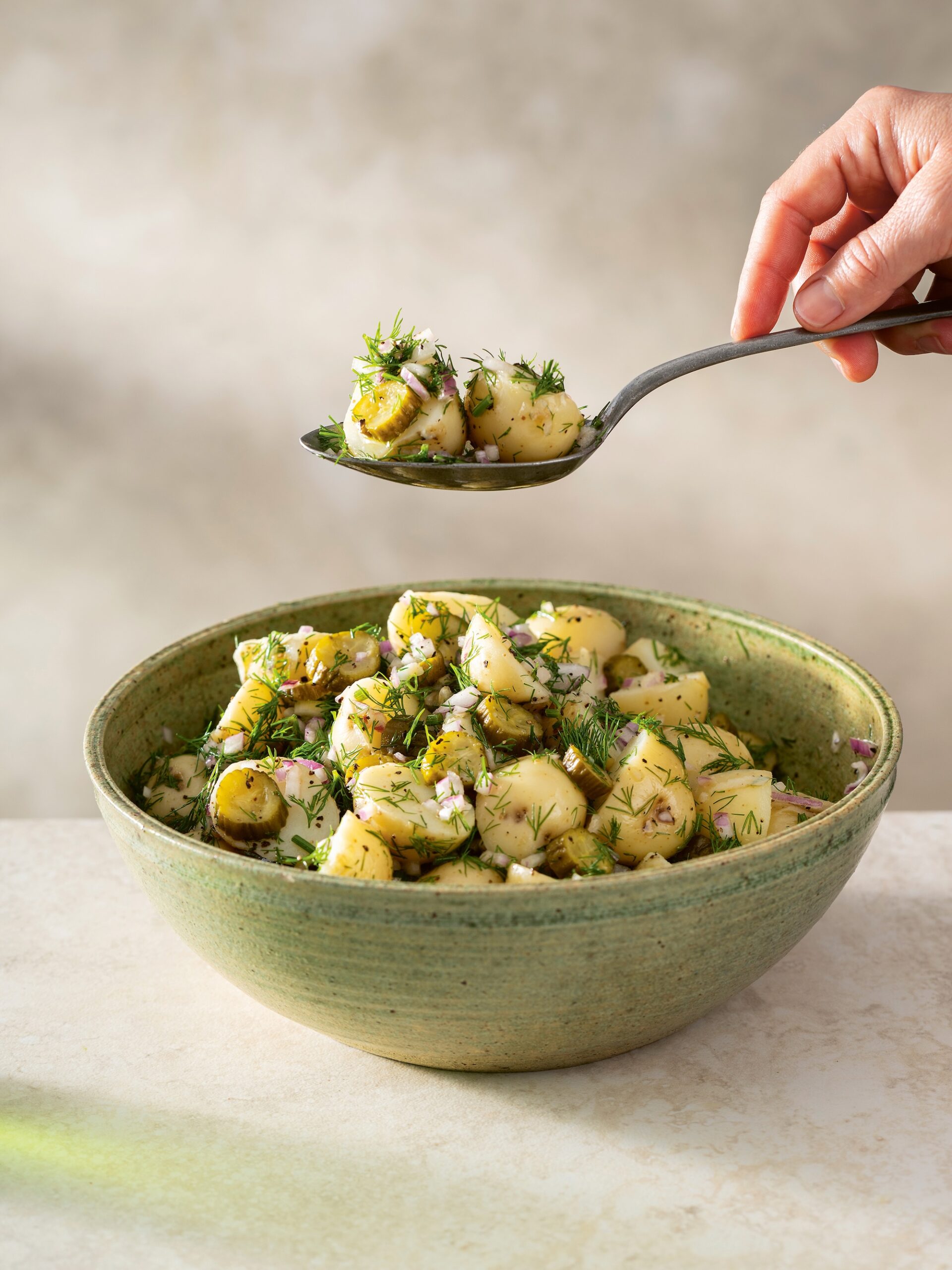 A green ceramic bowl filled with gnocchi and vegetables.