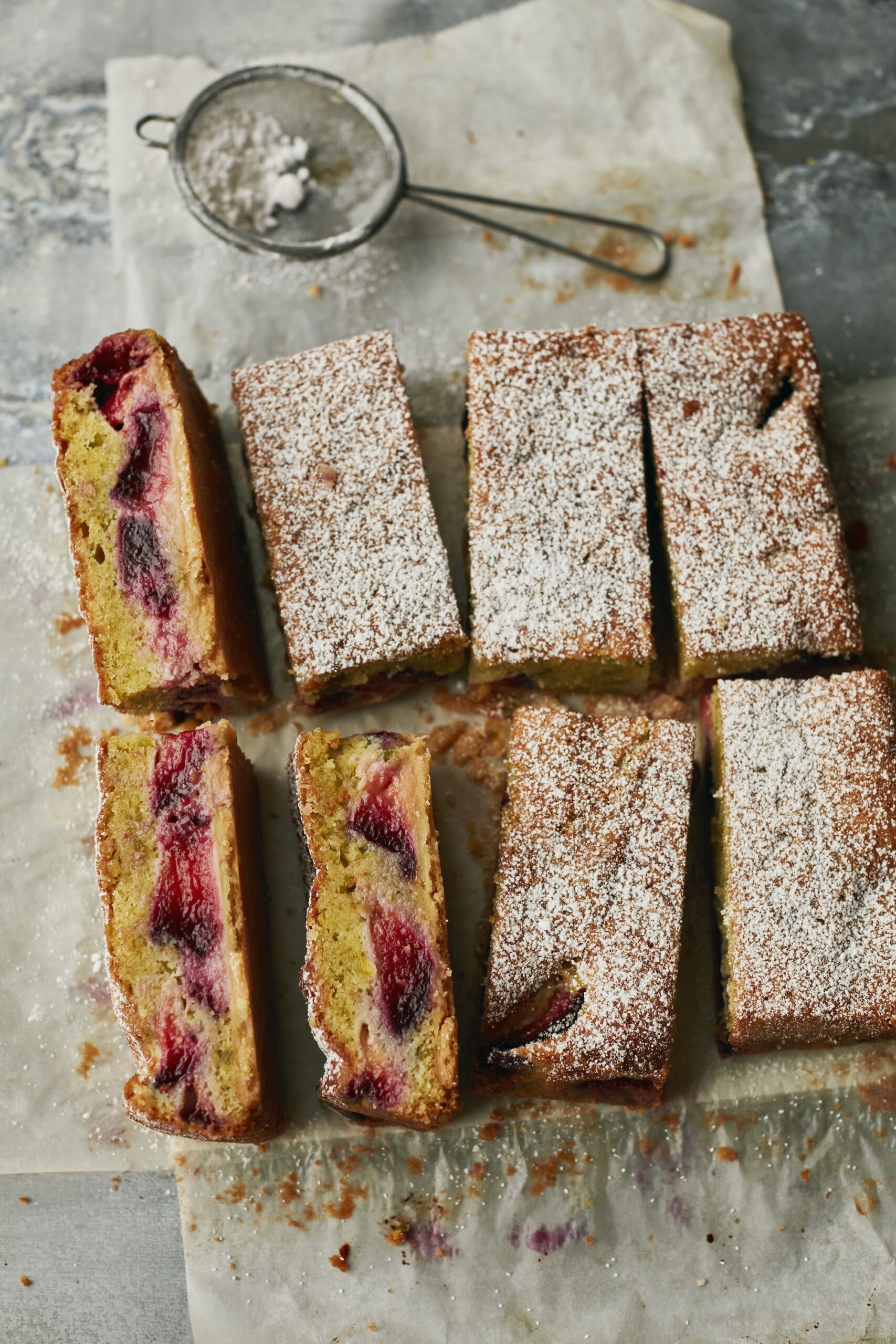 Plated slices of plum and pistachio cake dusted with powdered sugar