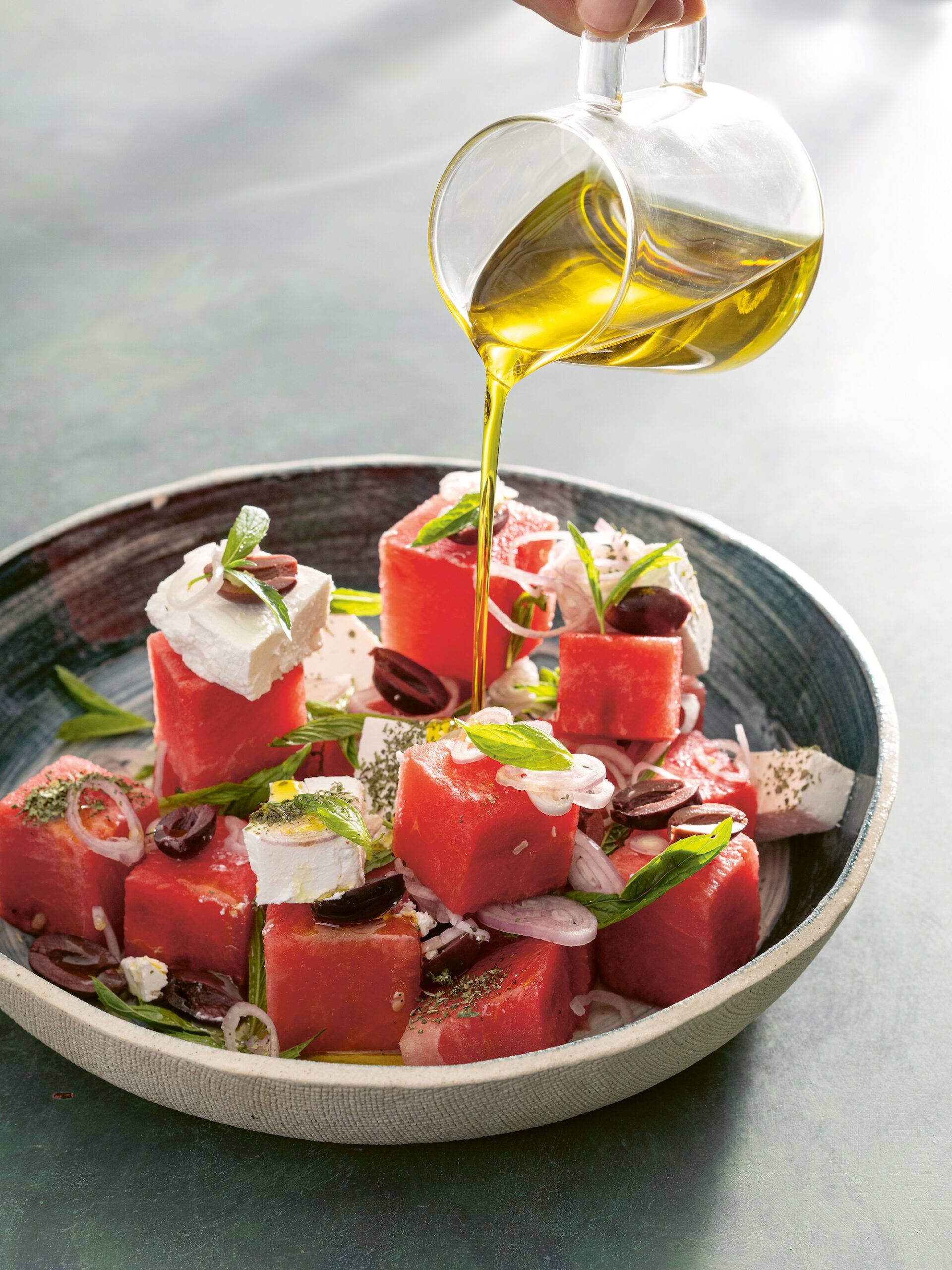 A bowl of watermelon cubes drizzled with olive oil and garnished with herb