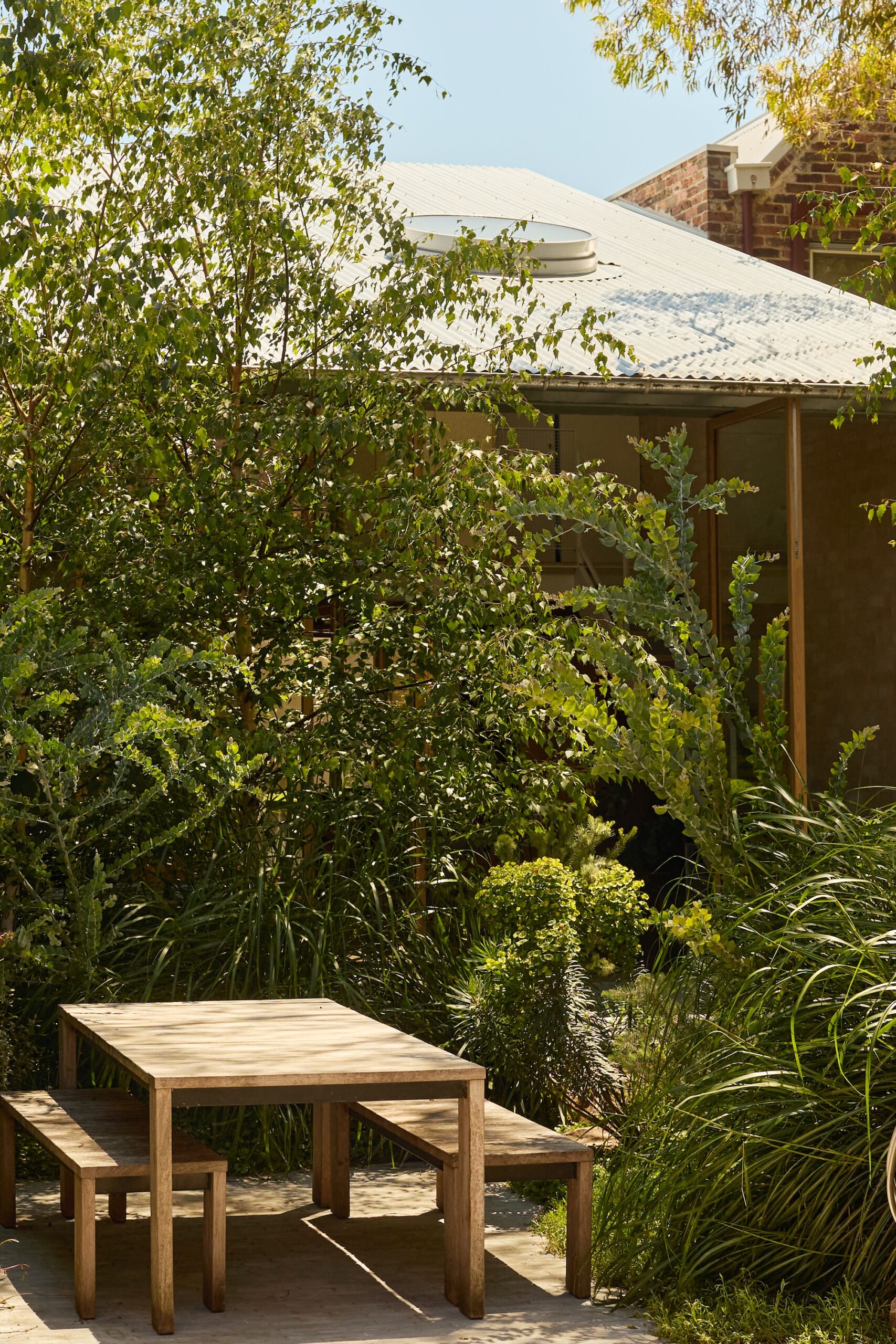 x Private green courtyard by Jala featuring layered planting and natural timber seating.
