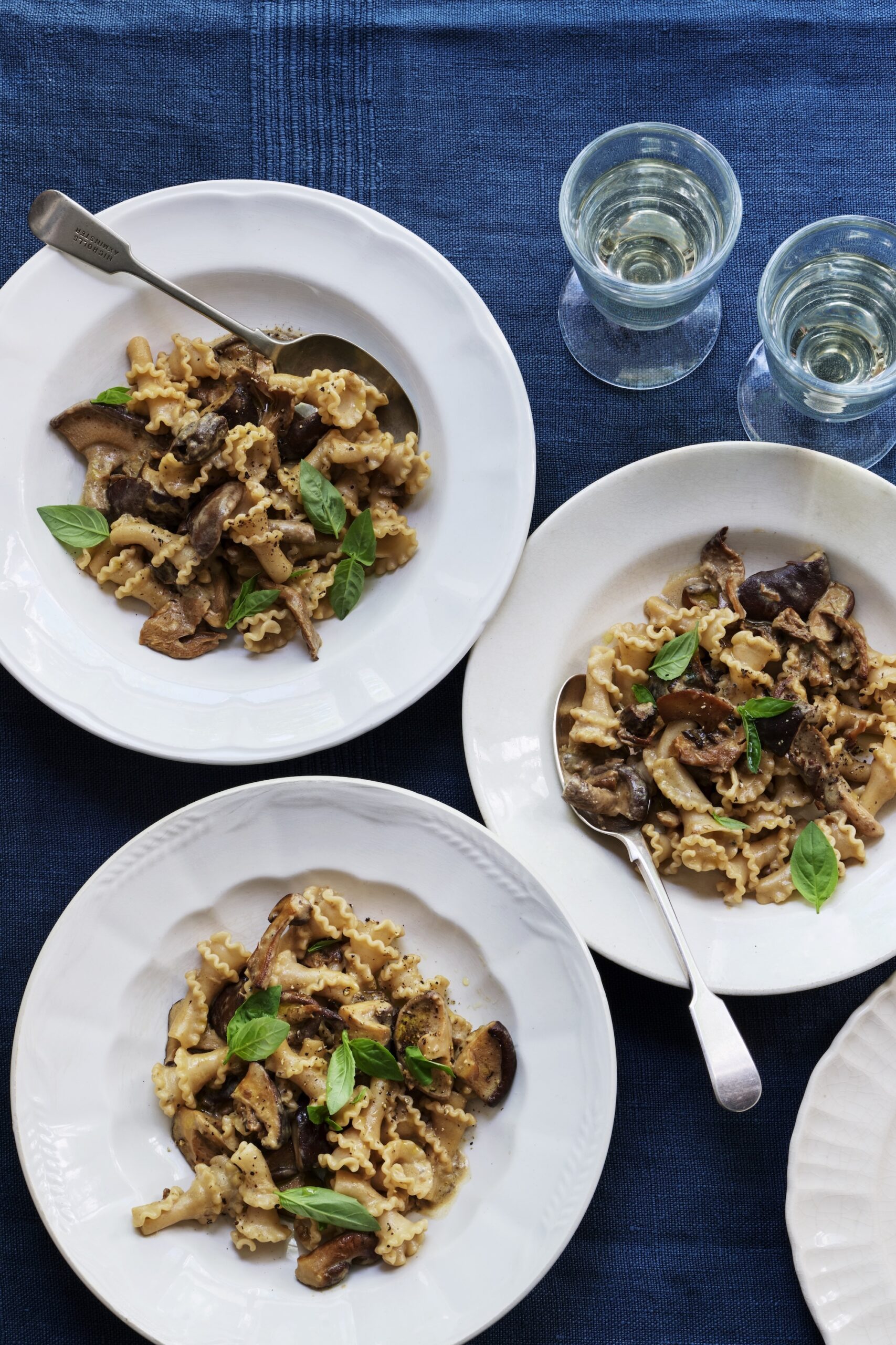 Three bowls of mushroom pasta served alongside white wine