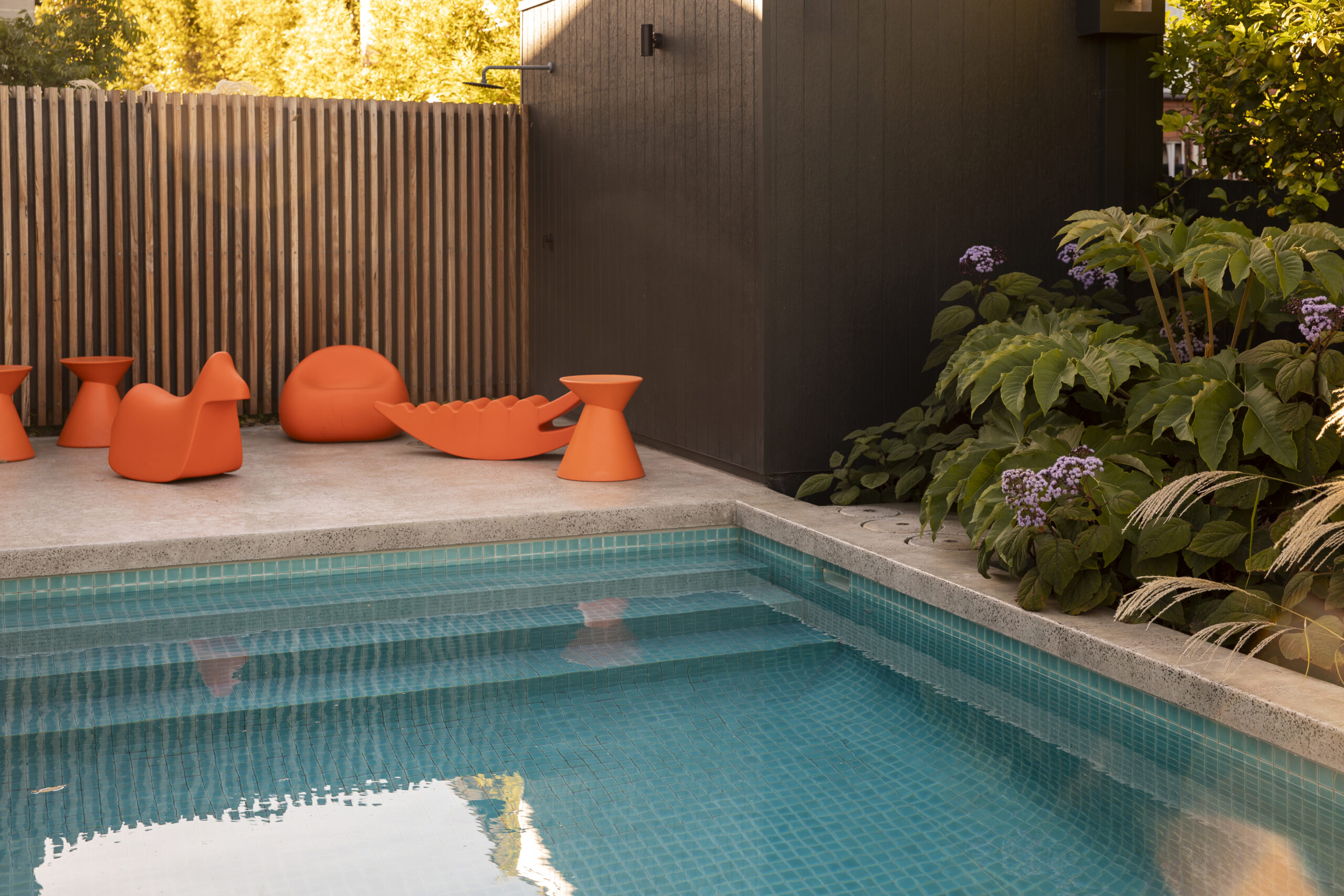 Bright orange modern furniture sits alongside pool and layered planting in Andy Murray Rosanna garden