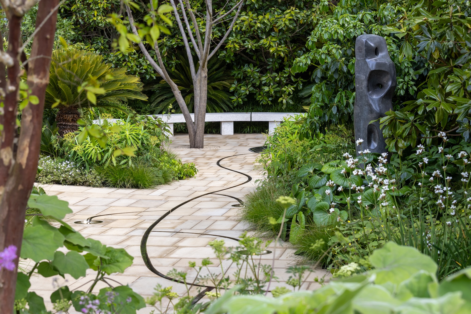 Contemporary sculpture beside a winding path leading to seating feature in RHS CFS The Tate Britain Garden.