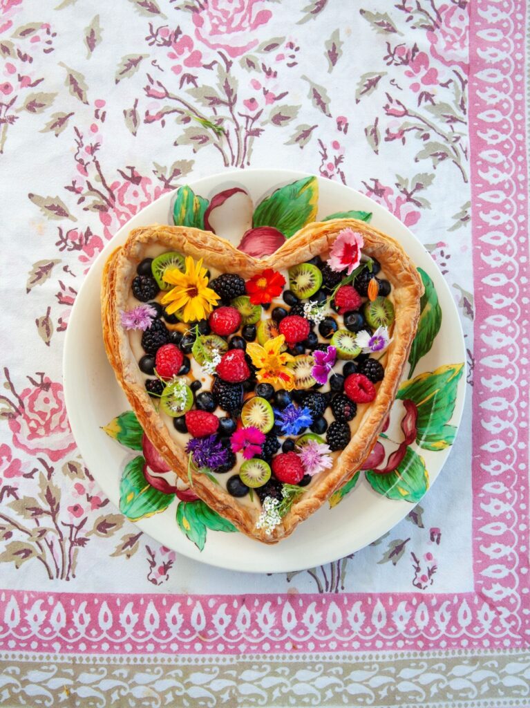 Heart-shaped fresh fruit tart served on colourful plate and table