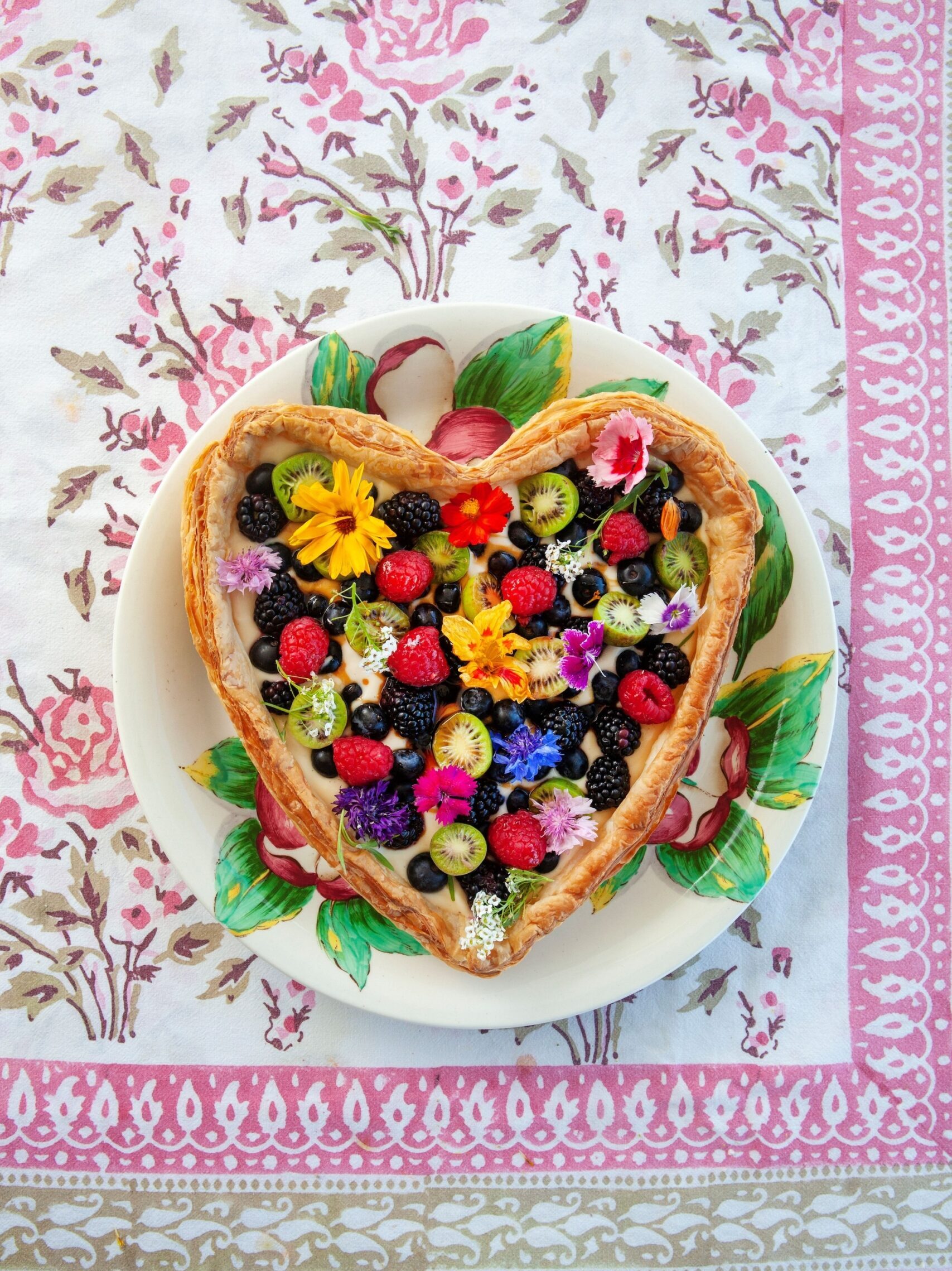 Heart-shaped fresh fruit tart served on colourful plate and table